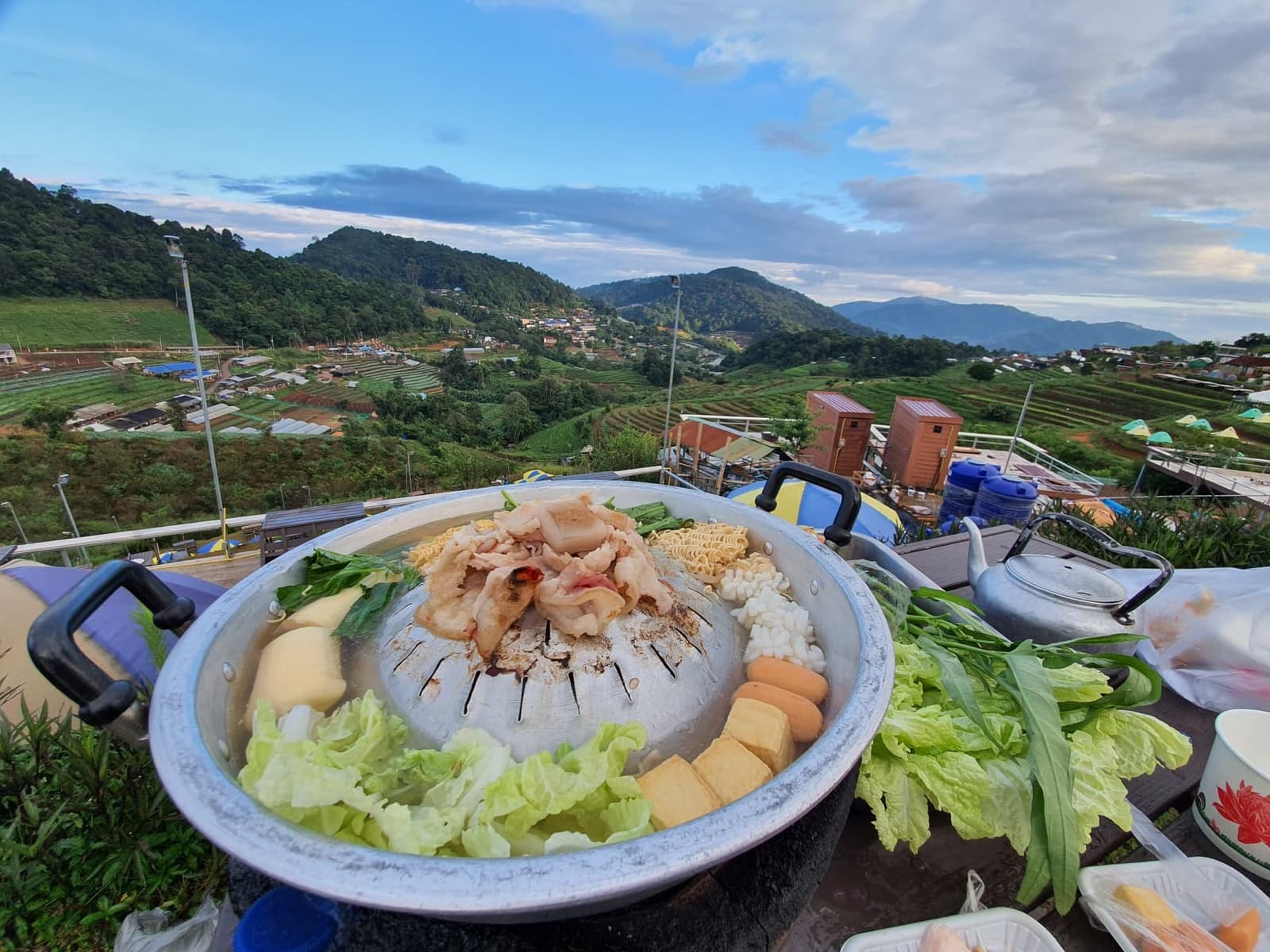 หม้อหมูกระทะบนโต๊ะ มองข้ามไปเห็นไร่ขั้นบันไดและทิวเขาที่ม่อนแจ่ม